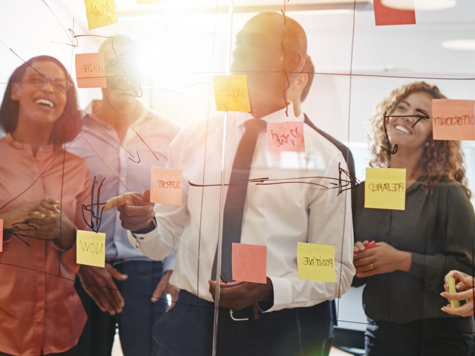 Young professionals brainstorming with sticky notes on a glass wall with his team while working together in a modern office